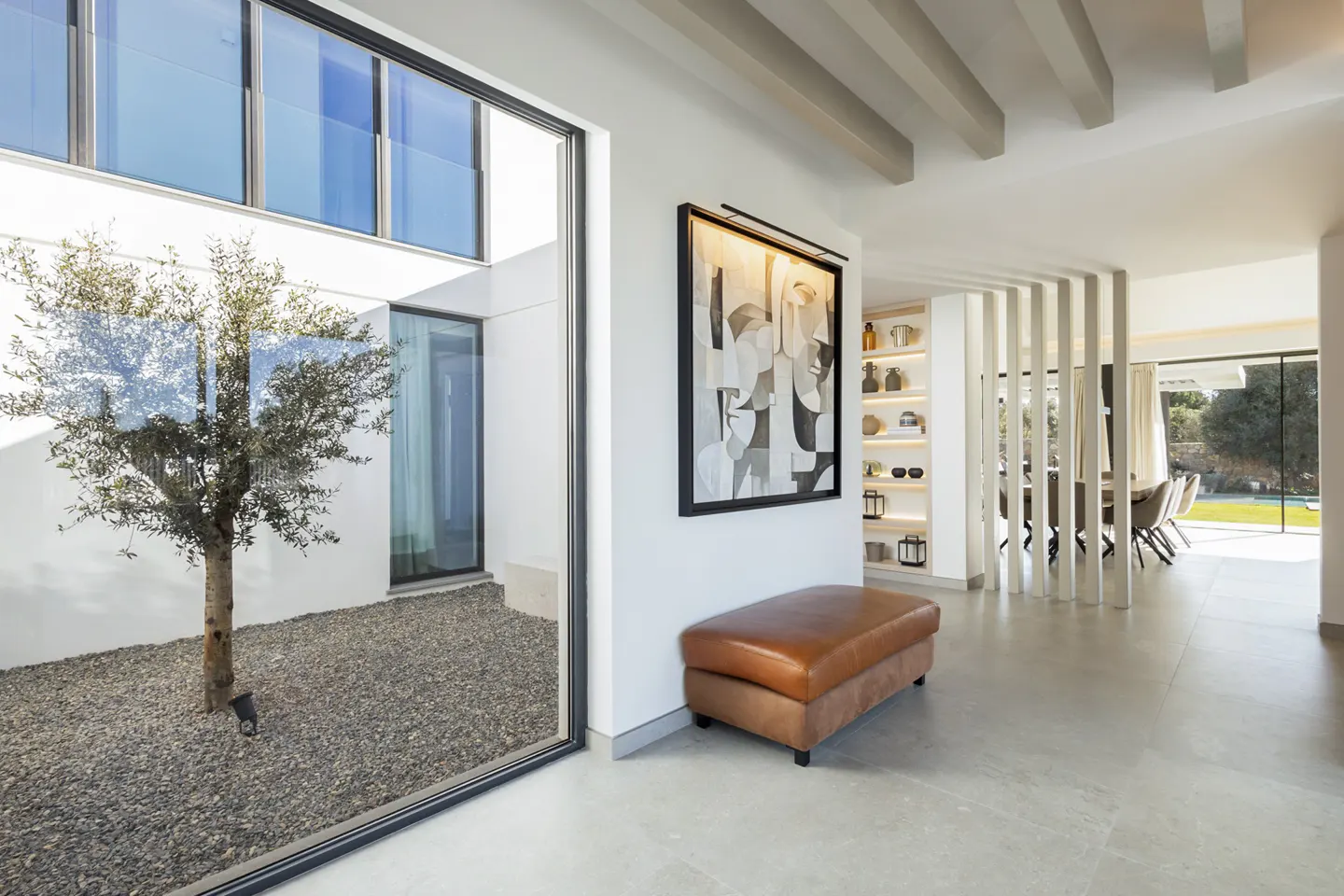 Modern interior with a leather bench, abstract art, and a view of an outdoor courtyard with an olive tree.