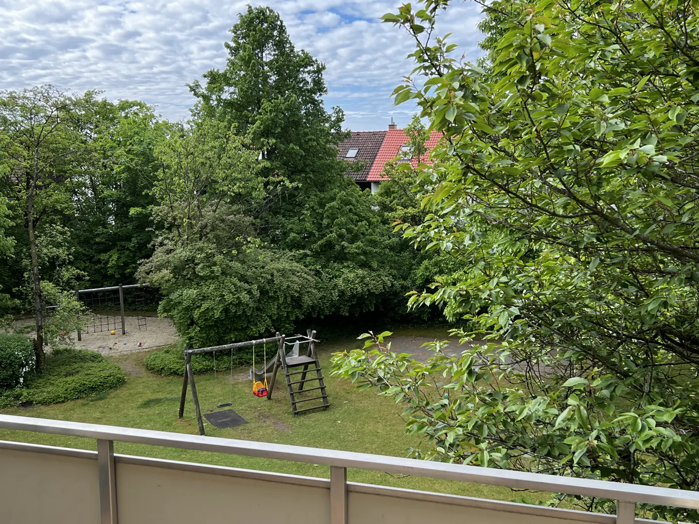 View from a balcony overlooking a lush green backyard with a wooden swing set, slide, and climbing frame.