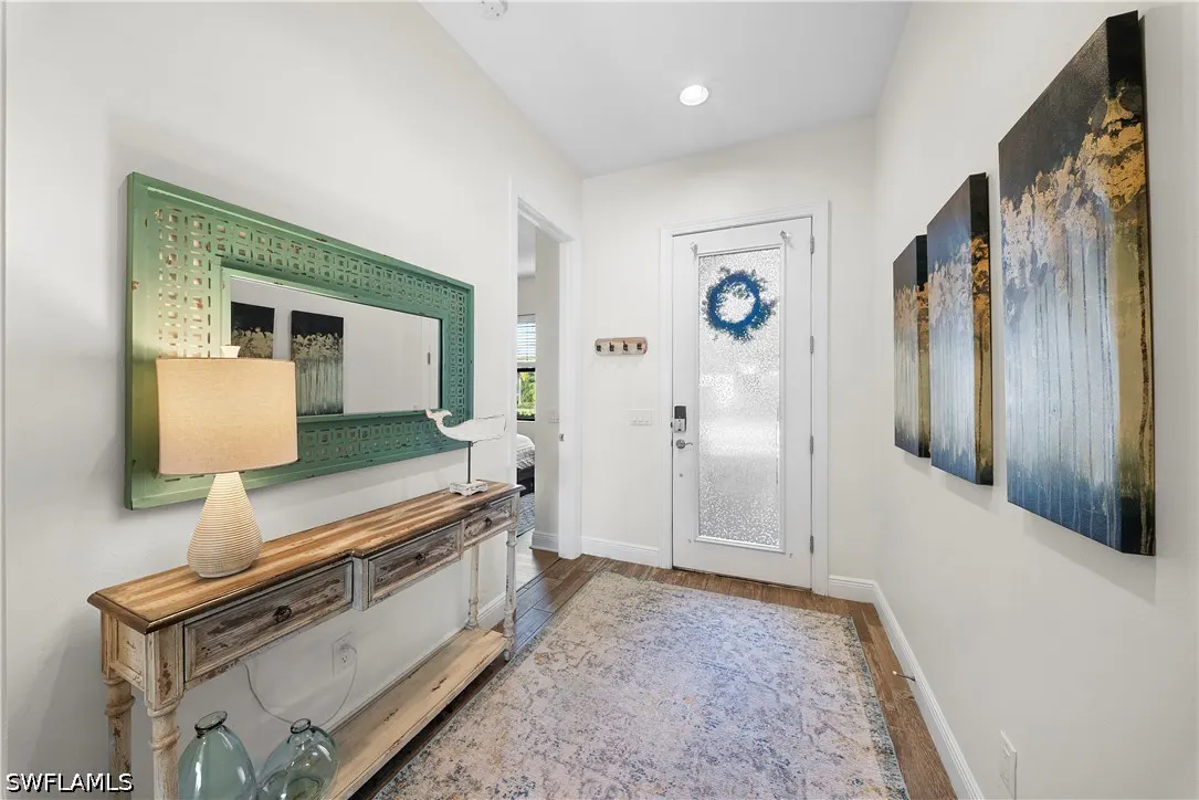 Bright entryway with a rustic wood console table, green mirror, table lamp, and three abstract blue and gold wall paintings.