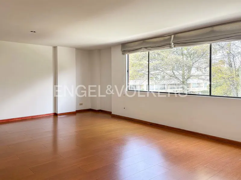 Empty room with hardwood floors, white walls, and a large window with a gray shade. Trees are visible outside. Engel & Volkers logo.