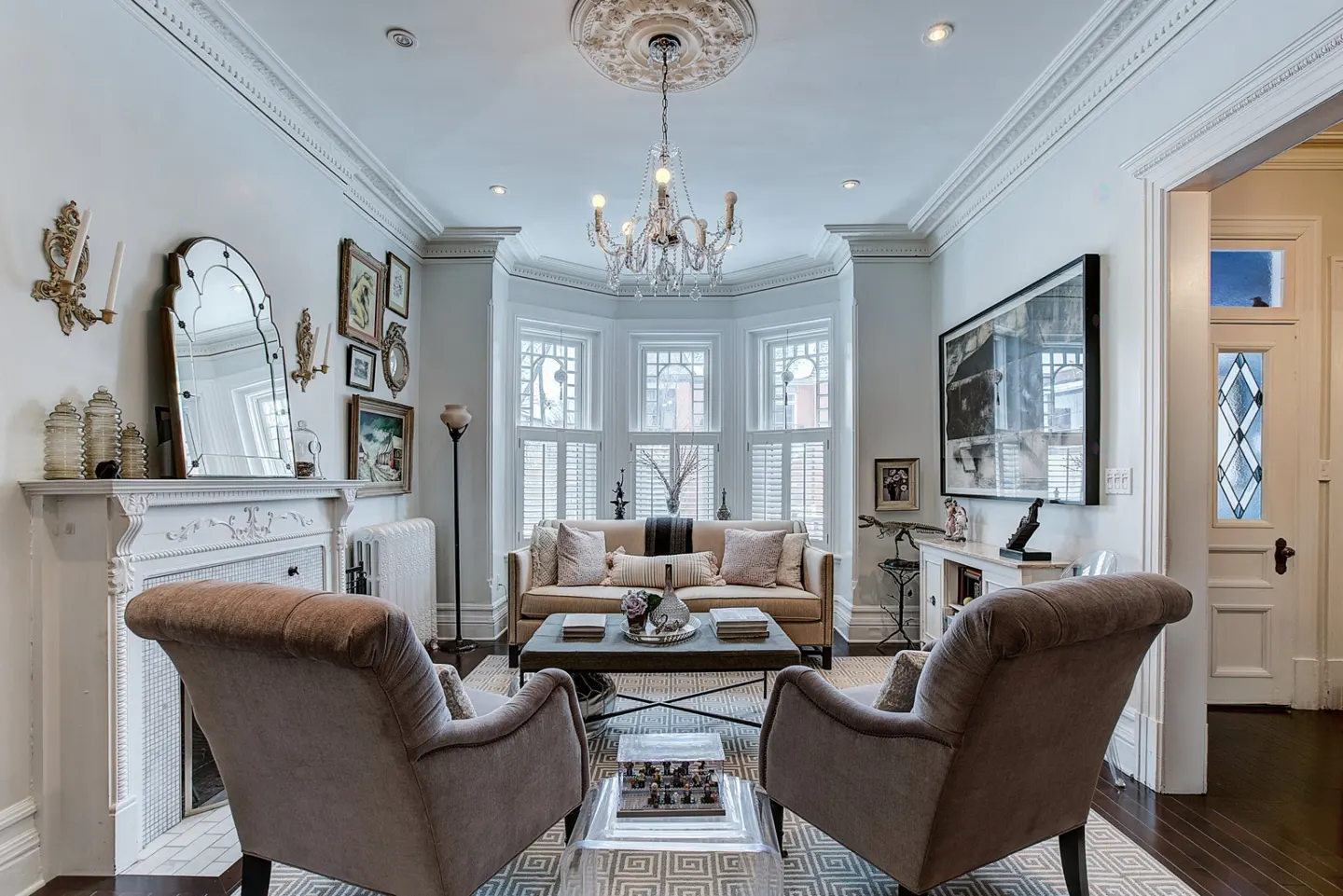 A living room with two armchairs, a sofa, and a coffee table. A chandelier hangs from the ceiling.