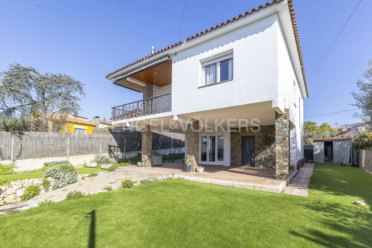 Two-story white house with stone accents, a balcony, and a green lawn on a sunny day.