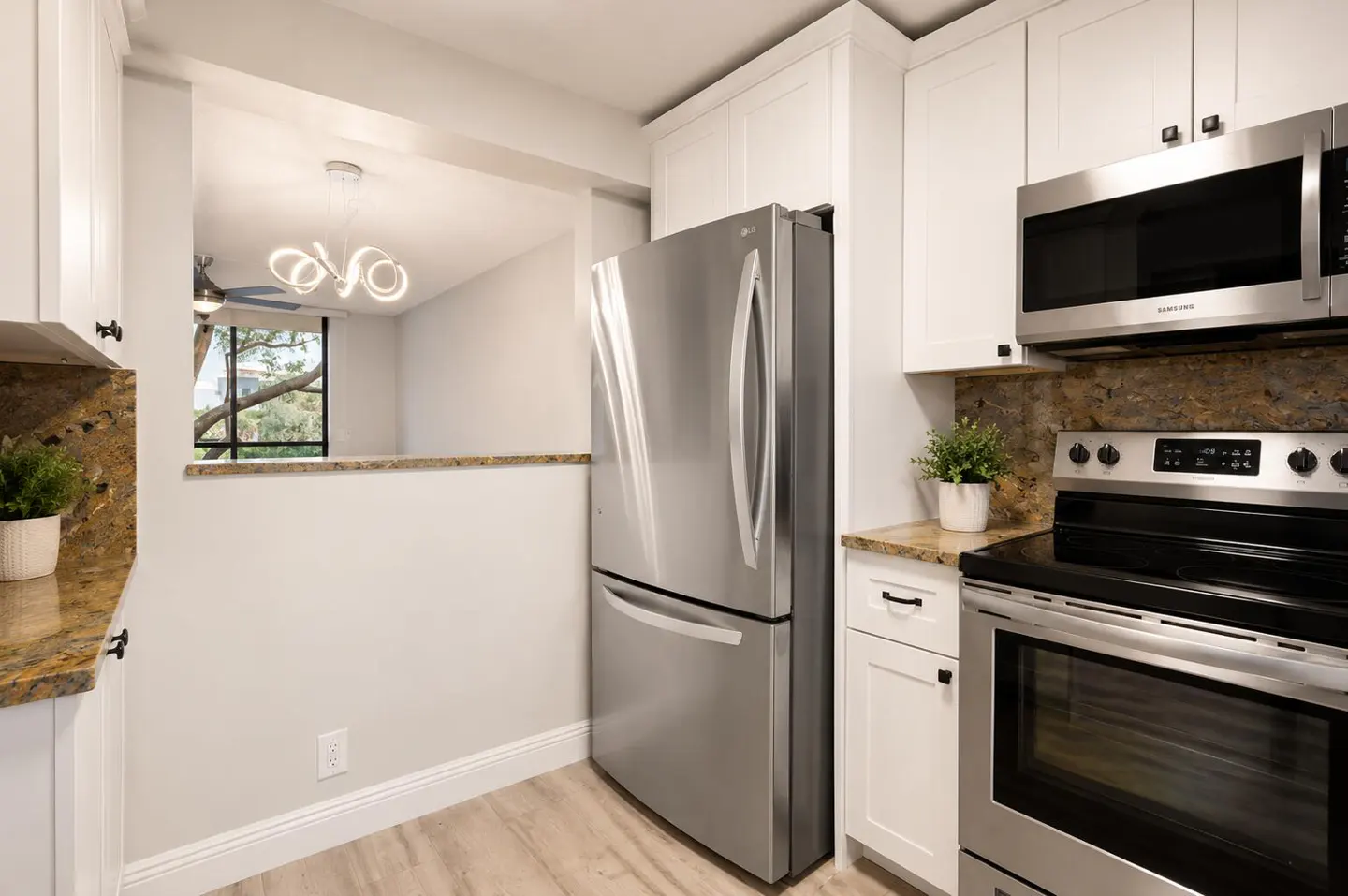 A kitchen with white cabinets, stainless steel appliances, and granite countertops. A pass-through to the living room is visible.