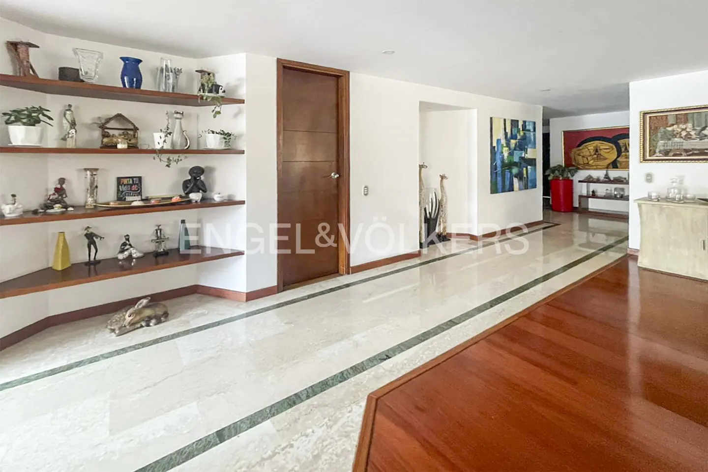 A bright hallway with marble floors, wooden accents, and decorative shelves.
