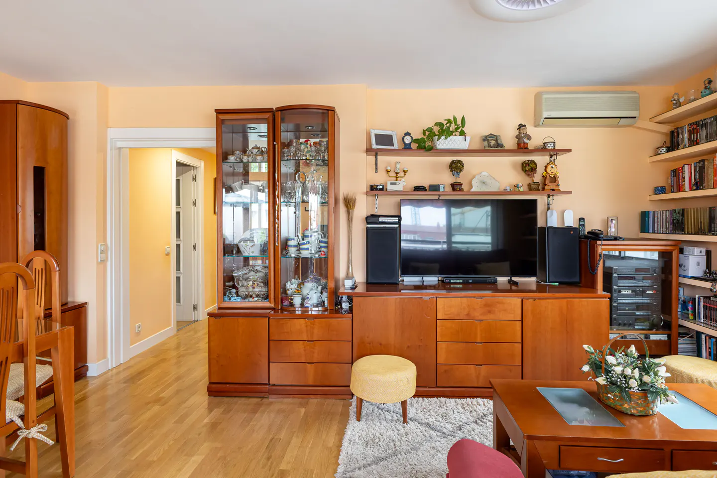 Living room with wood floors, peach walls, and wood furniture including a TV stand, display cabinet, and coffee table.