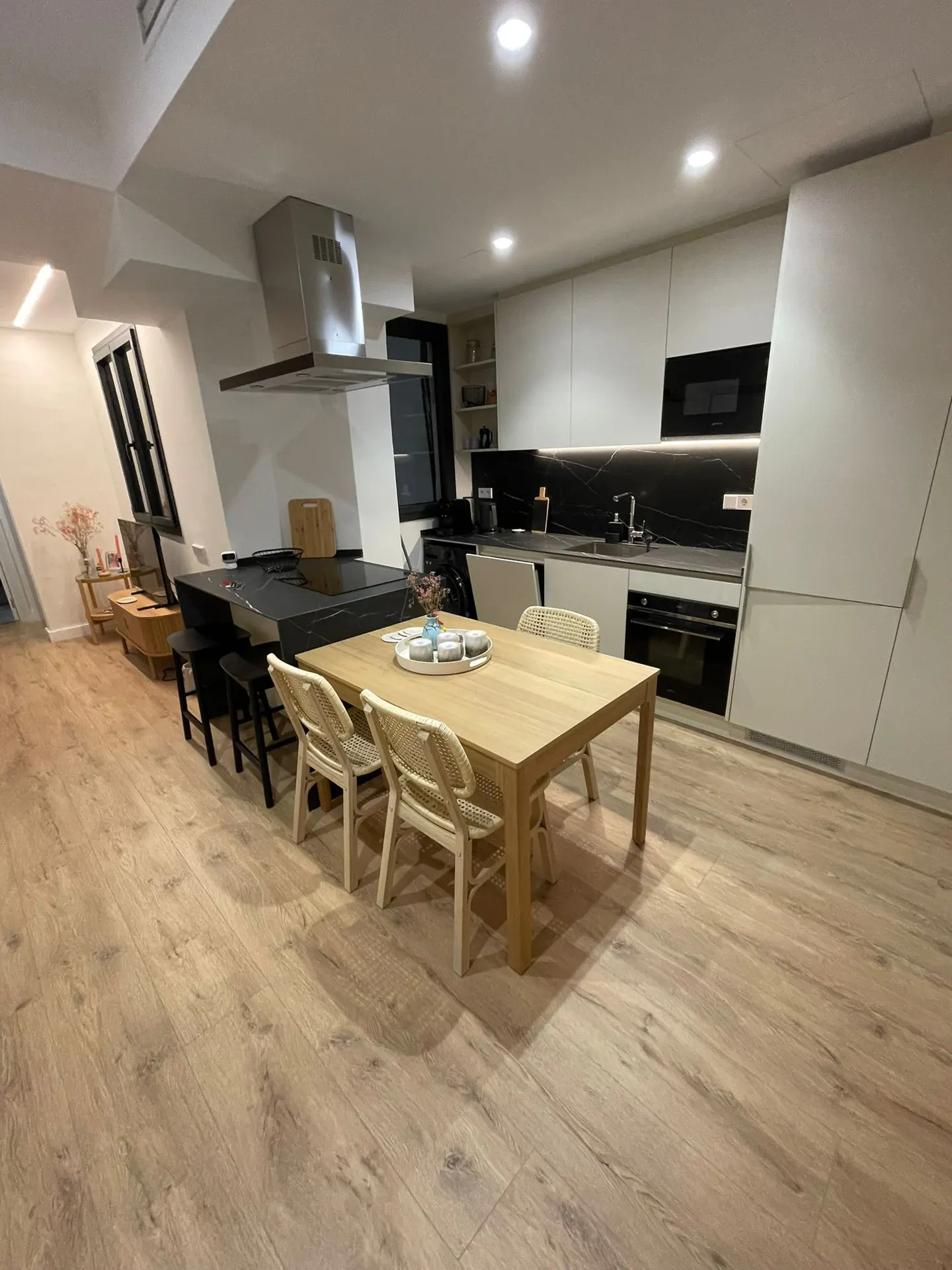 Modern kitchen with light wood floors, a wooden dining table, white cabinets, and a black marble backsplash.