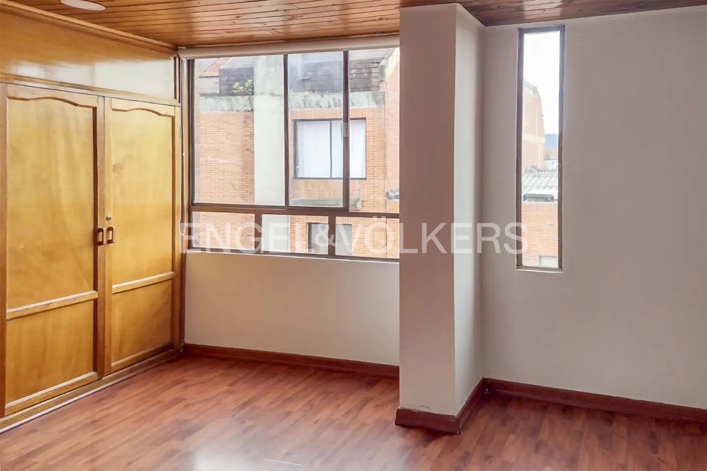 An empty bedroom with wood floors, a large window, and a wooden wardrobe.