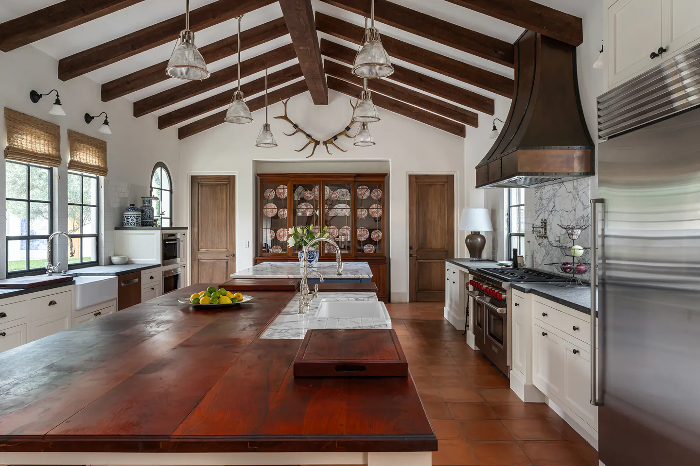 A bright kitchen with a large wooden island, white cabinets, and a copper range hood.