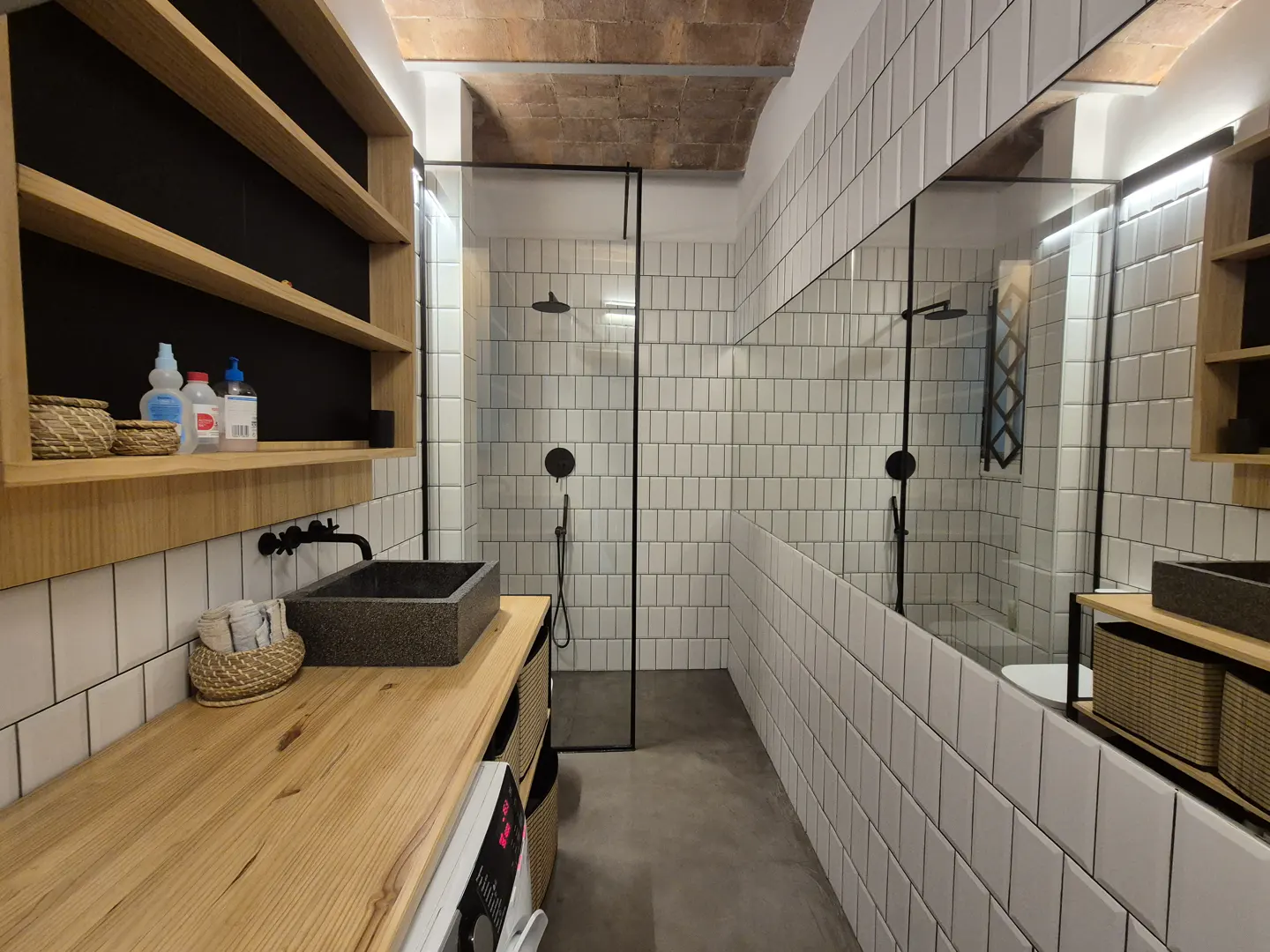 Modern bathroom with white subway tiles, black fixtures, and a wood countertop. A glass shower enclosure is visible.