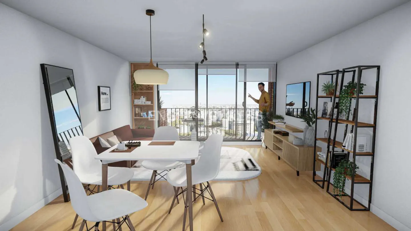 Bright apartment interior with white walls, wood floors, and city view. A man stands on the balcony. Table and chairs in the foreground.