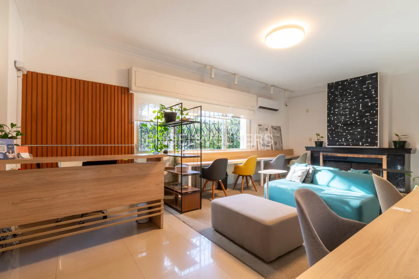 Bright, modern office space with a blue sofa, fireplace, and wood accents. Desks line the window.
