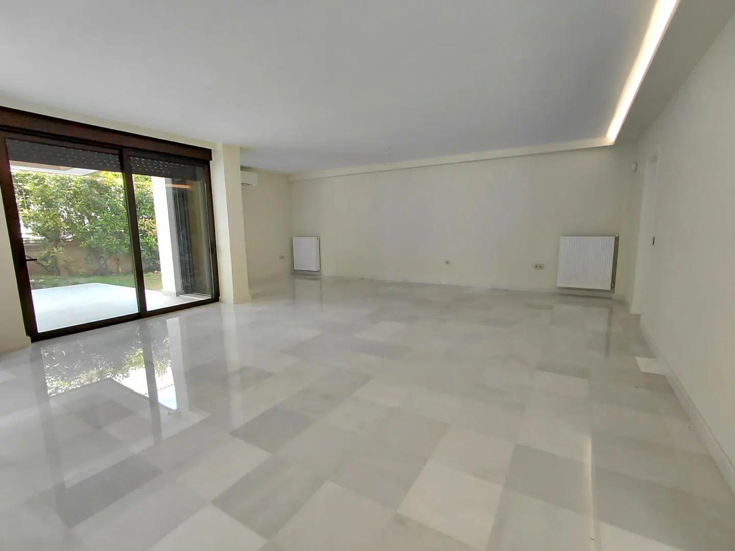 Bright, empty room with marble floors and white walls. Large sliding glass doors lead to a green yard.