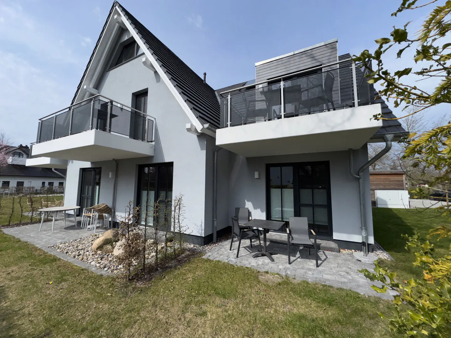 Exterior view of a modern gray house with black trim, balconies, and outdoor seating on a sunny day.