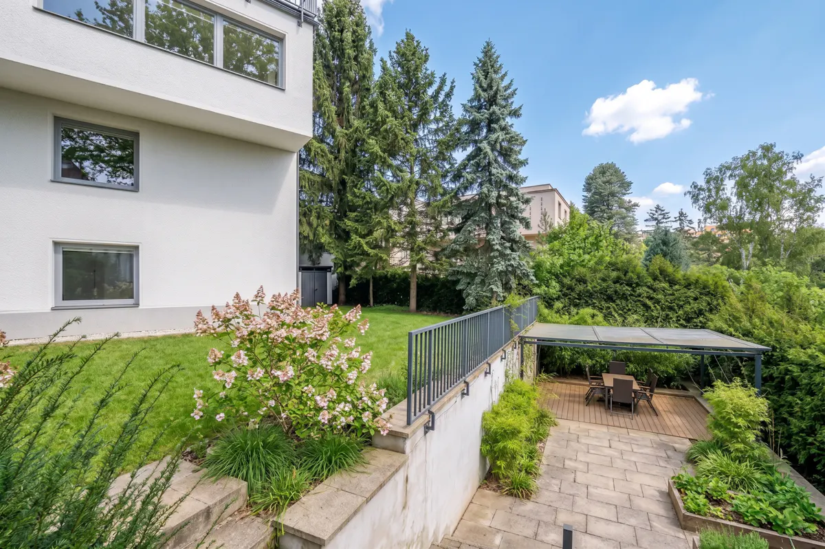 A modern white building with a lush green backyard, featuring a patio with a table and chairs.