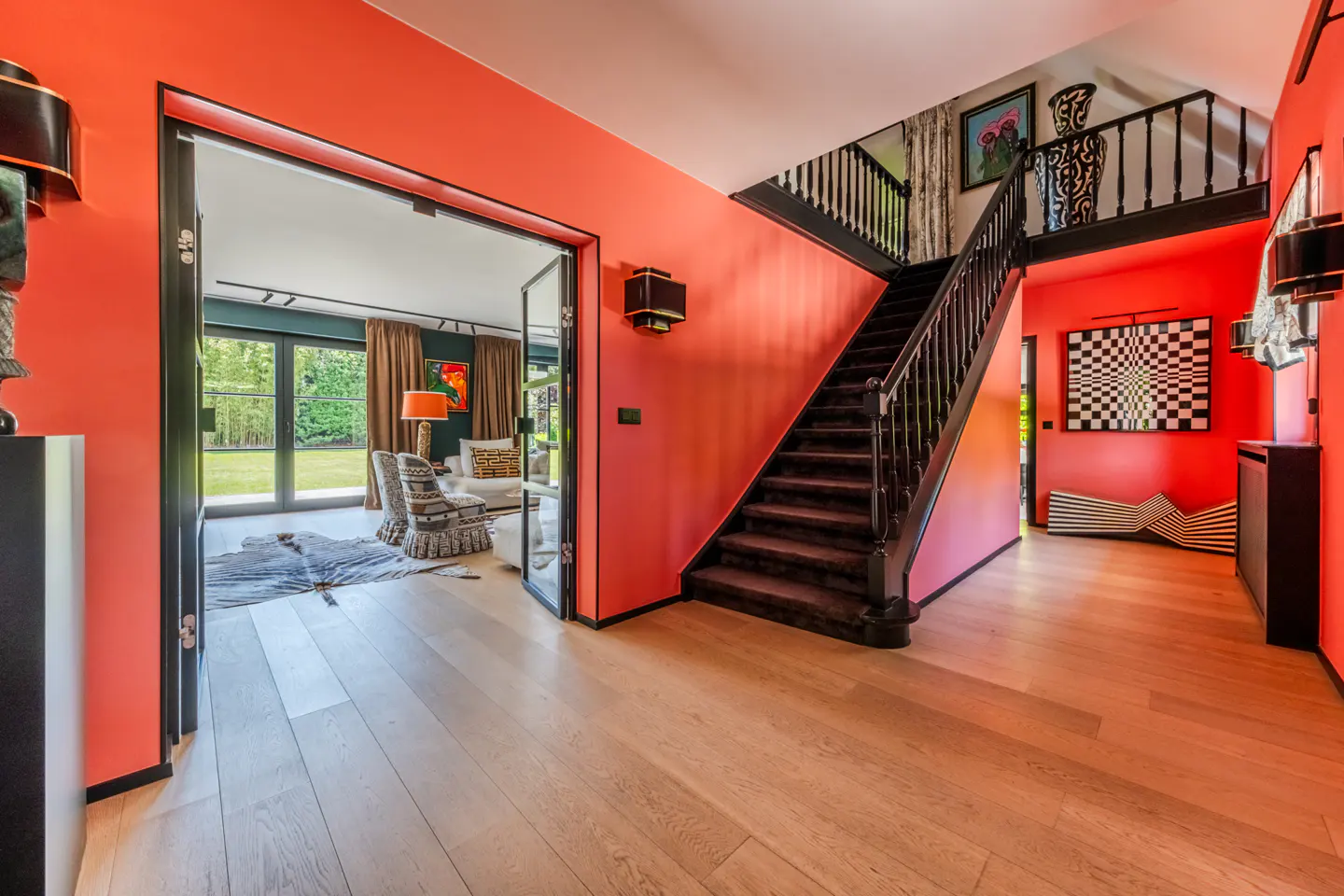Bright foyer with coral walls, light wood floors, and black trim. A staircase leads up, and a doorway shows a living room with a cowhide rug.