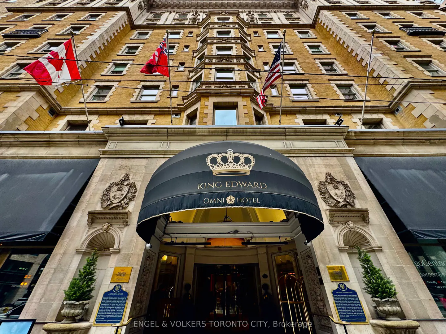 Exterior shot of the King Edward Omni Hotel with flags, a black awning, and a stone facade.