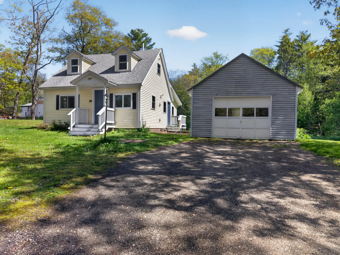 Yellow house with white trim, dormer windows, and a detached gray garage set on a grassy lot with a paved driveway.