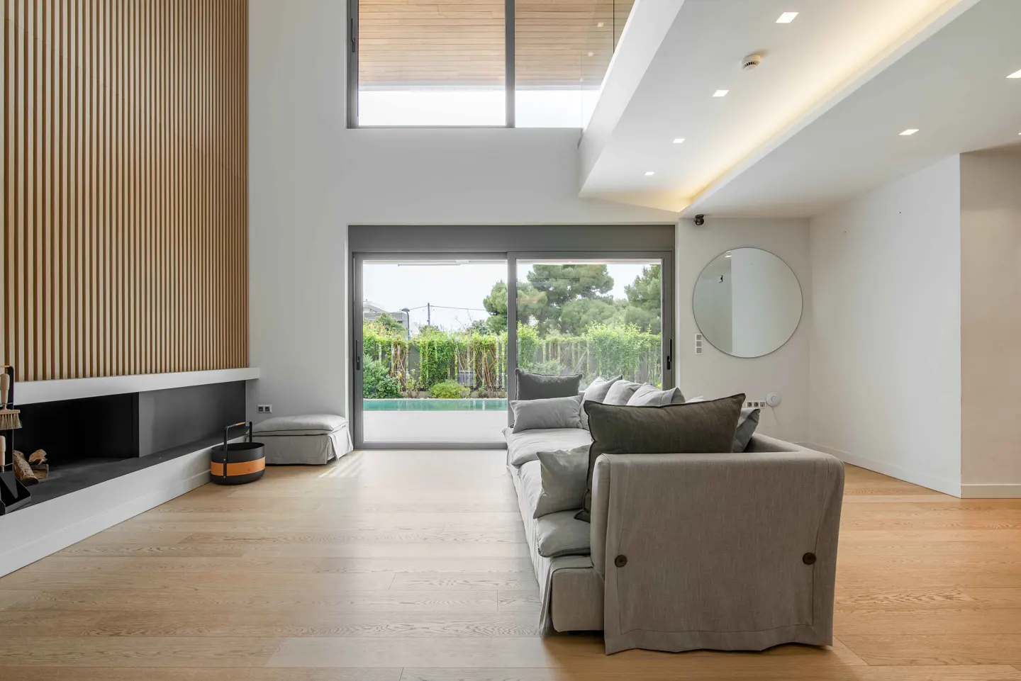 Bright living room with wood floors, a gray sofa, and a black fireplace under a wood slat wall. Sliding glass doors lead to a pool.