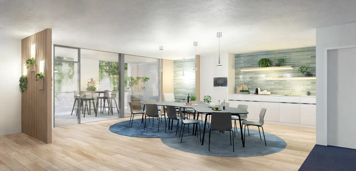 Bright, modern dining area with a long table, gray chairs, and a blue rug. A kitchen area with white cabinets and green tile is in the background.