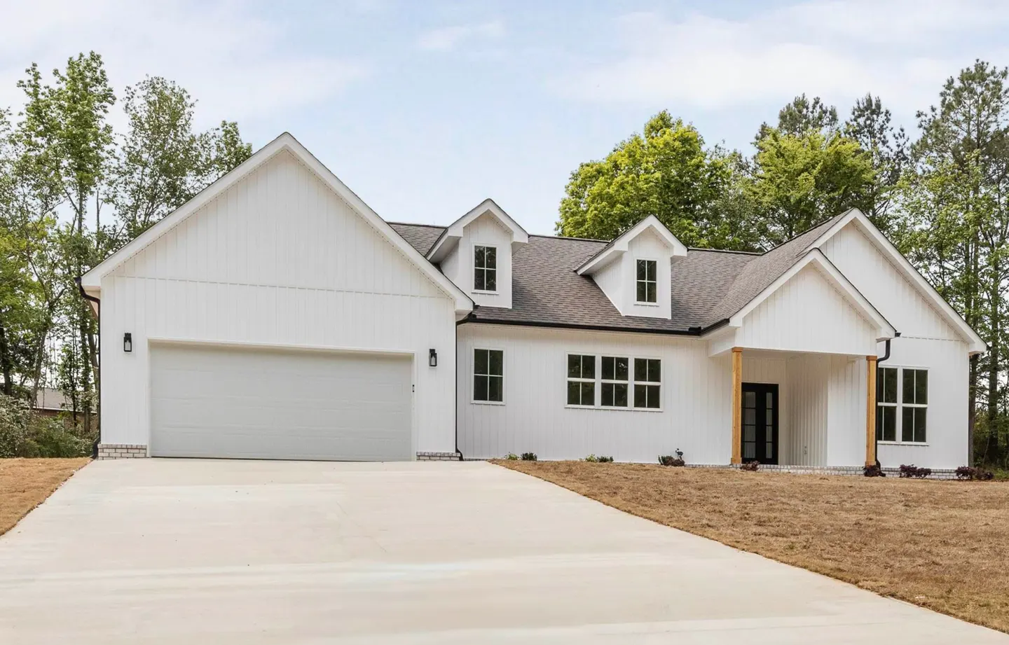 A modern, white farmhouse with a gray roof, black windows, and a concrete driveway. Trees are in the background.
