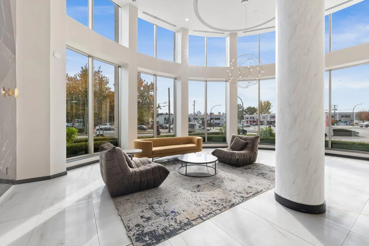 Bright lobby with floor-to-ceiling windows, marble floors, and modern furniture. A yellow sofa and gray chairs sit on a patterned rug.