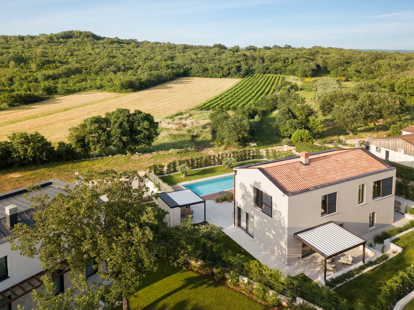 Aerial view of a modern two-story house with a red tile roof, a pool, and a vineyard in the background.