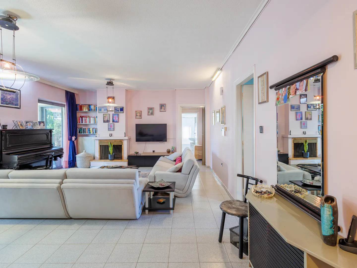 A bright living room with pink walls, a white sectional sofa, a black piano, and a fireplace.