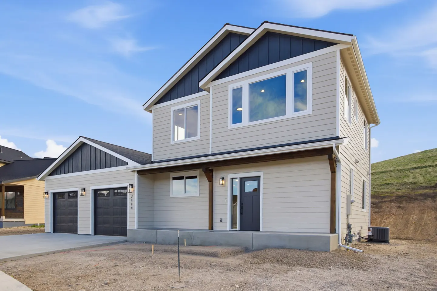 Two-story beige house with a dark gray roof and a two-car garage under a blue sky.