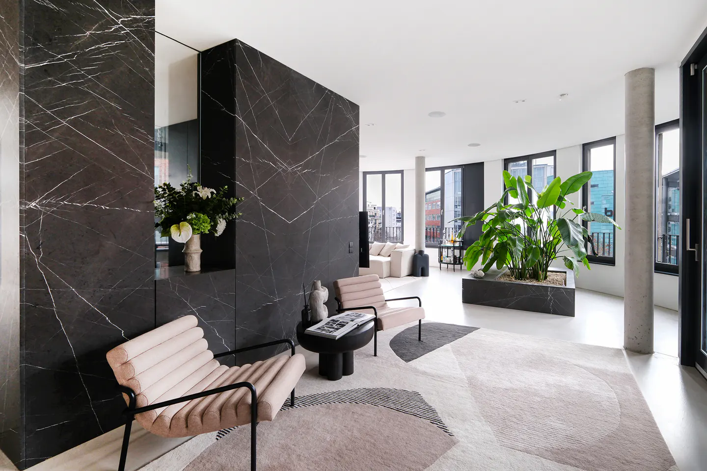 Bright, modern living room with black marble accent wall, pink chairs, and large potted plant near curved windows.