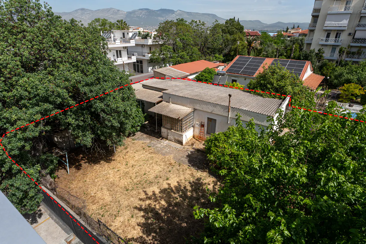 Aerial view of a property with a red dotted line marking its boundary, surrounded by trees and buildings.