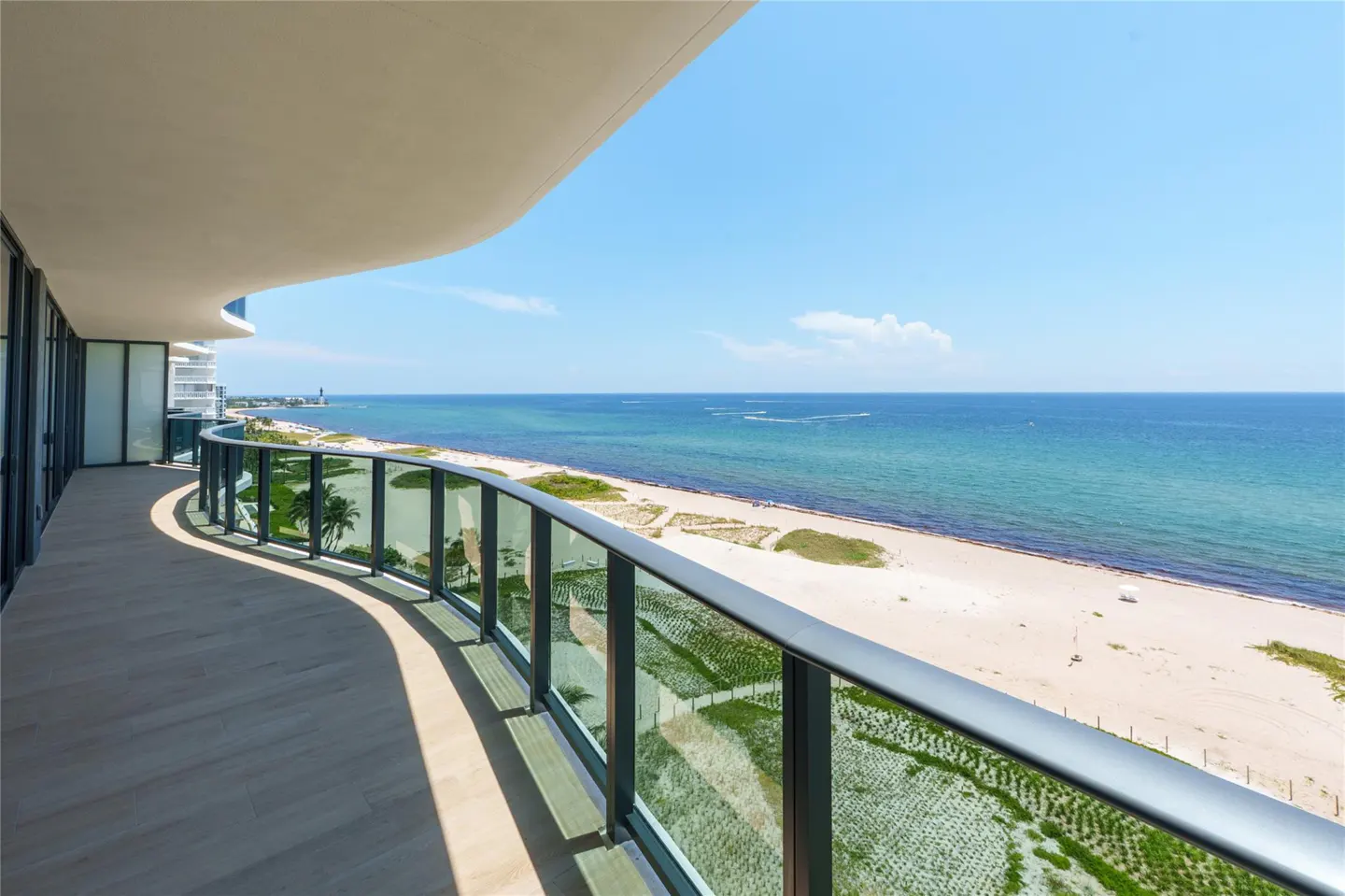Ocean view from a condo balcony with glass railings. The beach is sandy and the sky is blue.