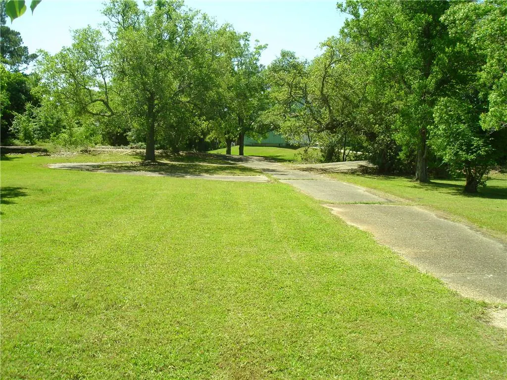 A long driveway leads to a house, surrounded by green grass and trees.
