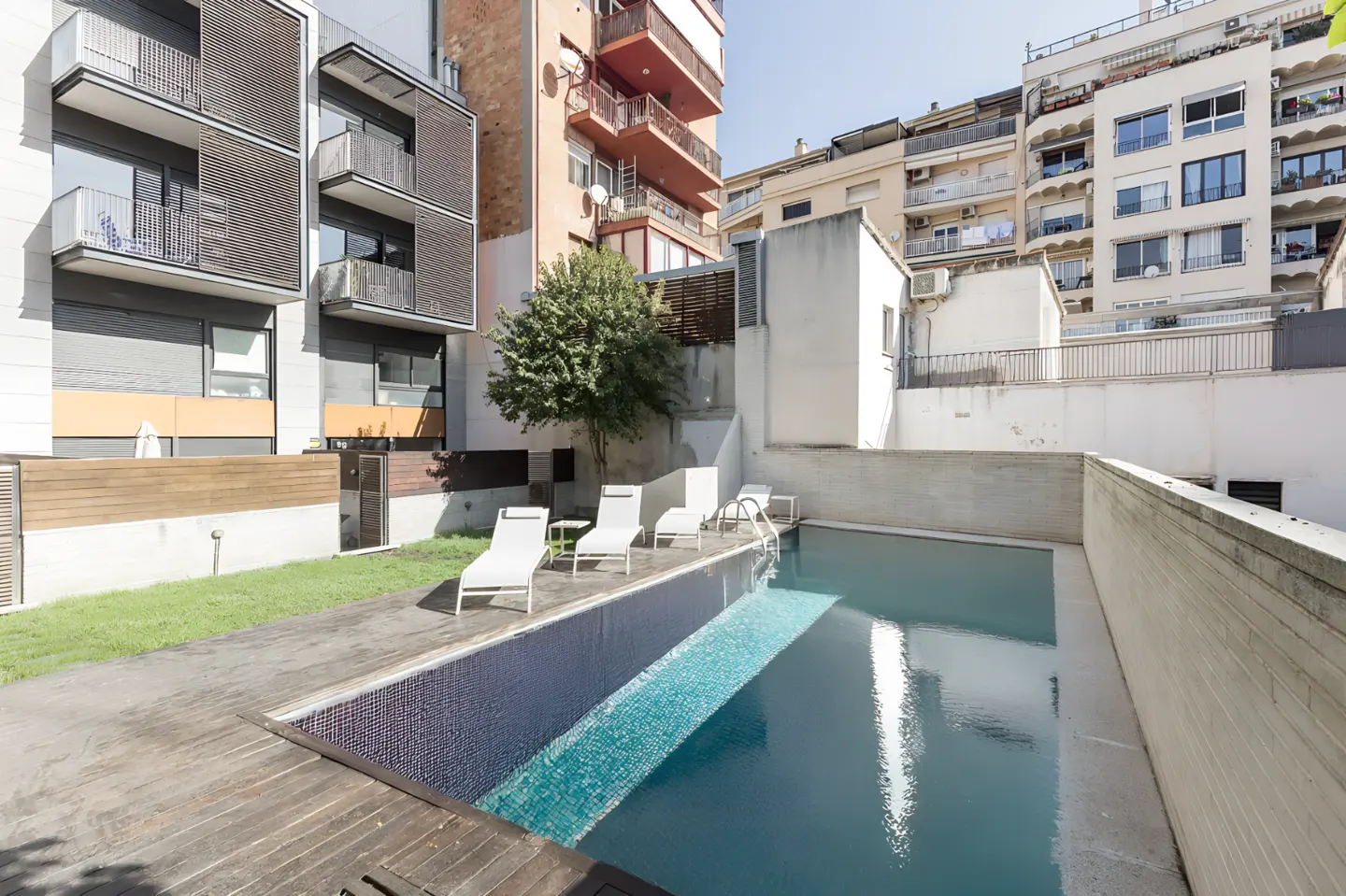 Outdoor pool with lounge chairs, surrounded by buildings. The pool has blue tile and clear water.
