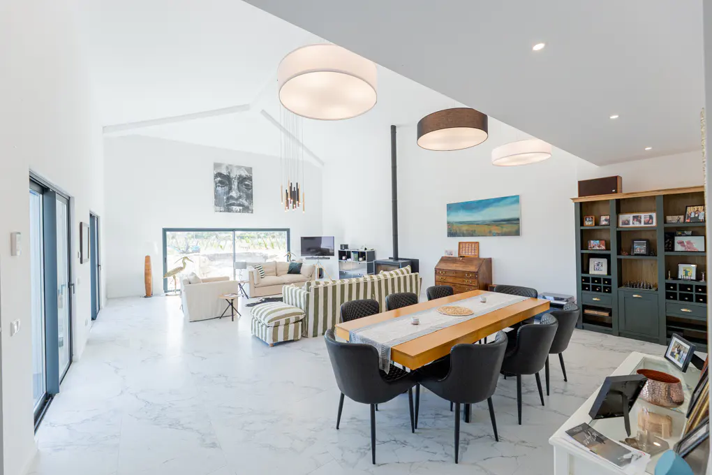 Bright, open-concept living space with white walls, marble floors, and high ceilings. Features a dining table, sofas, and a fireplace.