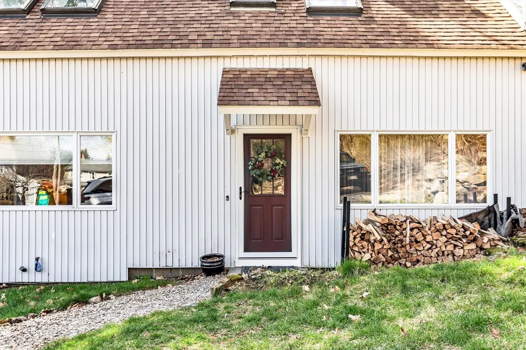 Exterior of a white house with a brown door, wreath, and wood pile.