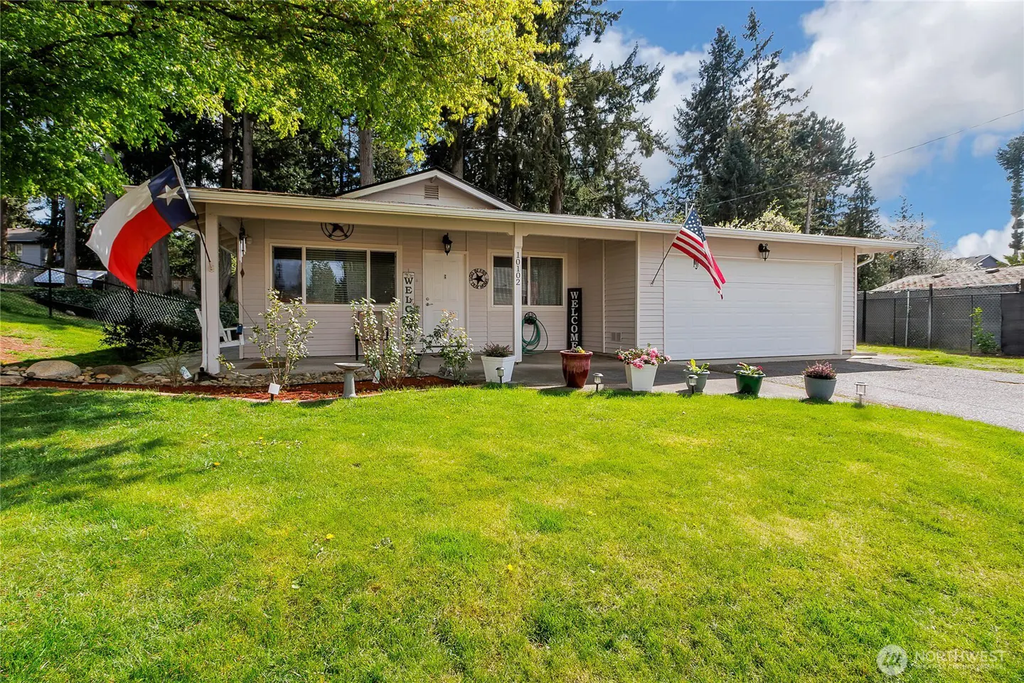 A single-story house with a green lawn, flower pots, and American and Texas flags.