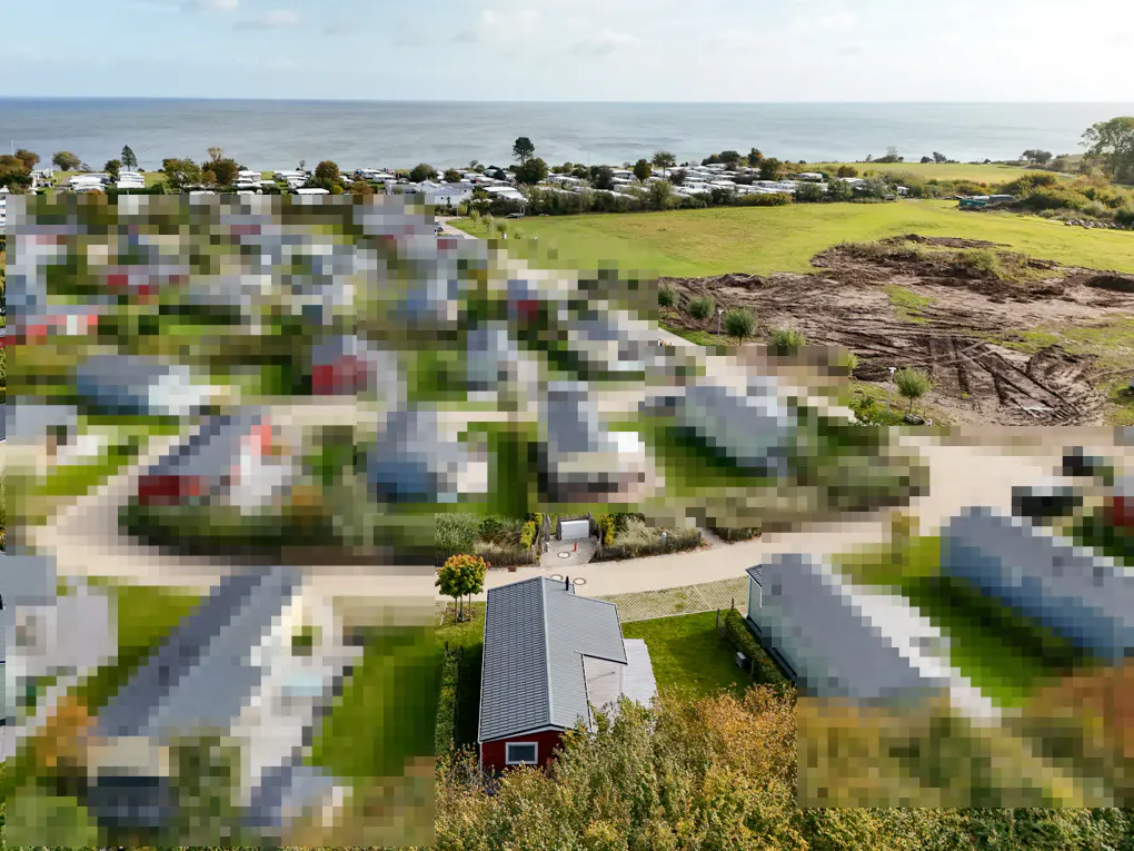 Aerial view of a coastal community with small houses, green lawns, and the ocean in the background.