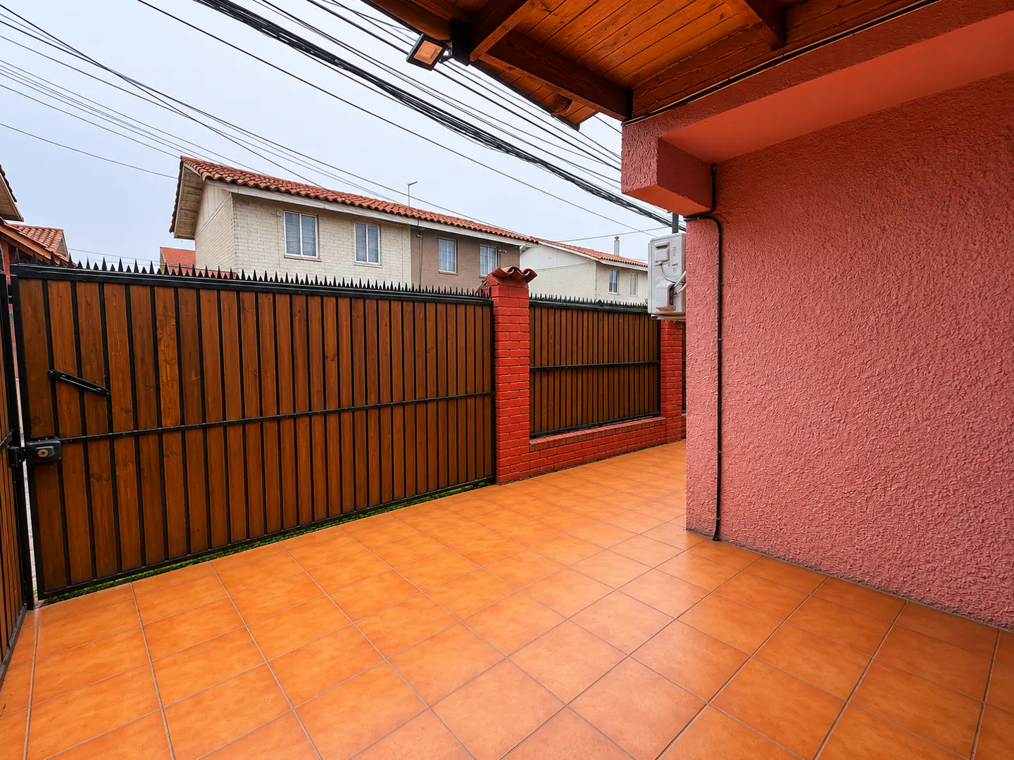 Exterior shot of a patio with orange tile, a wooden fence with black spikes, and a pink stucco wall.