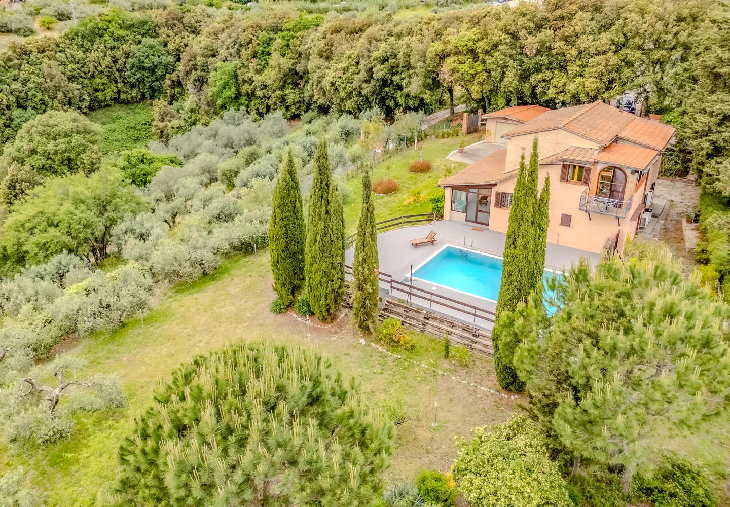 Aerial view of a peach-colored house with a red tile roof, a blue pool, and green trees.
