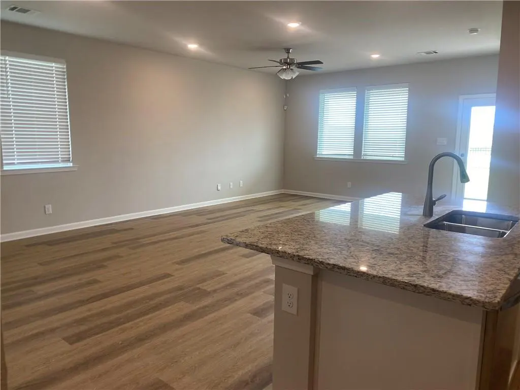 A bright, open-concept living space with wood floors, neutral walls, and a granite kitchen island with a stainless steel sink.