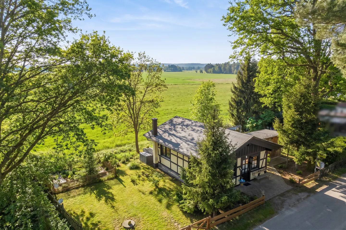 Aerial view of a half-timbered house with a green lawn, trees, and a field in the background on a sunny day.