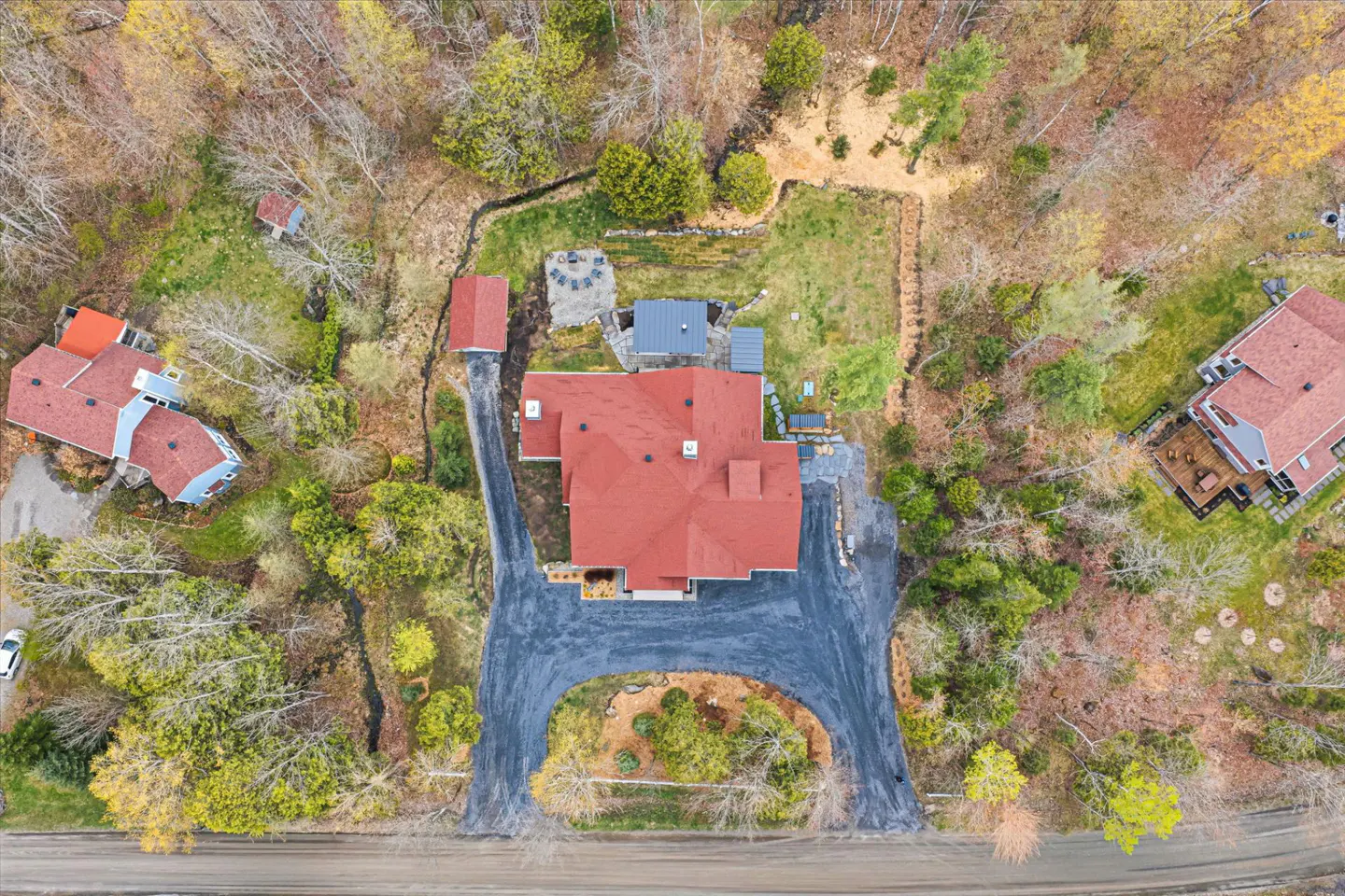 Aerial view of a house with a red roof, surrounded by trees and a driveway.