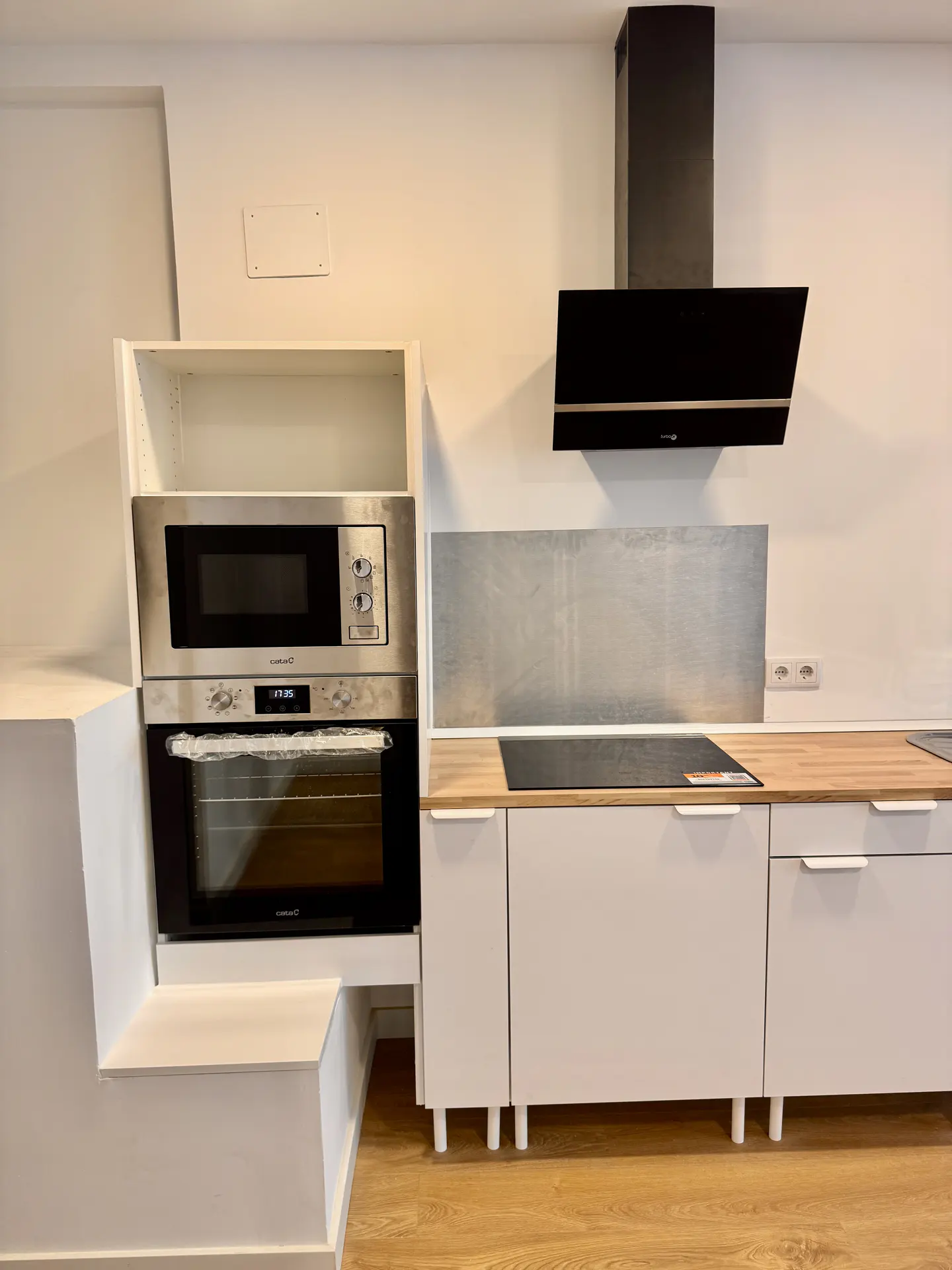 Modern kitchen with white cabinets, wood countertop, stainless steel microwave and oven, and a black range hood.