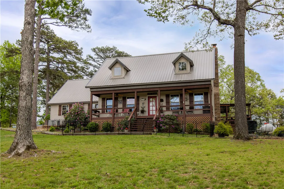 Tan house with a metal roof and a brown porch, surrounded by green grass and trees.