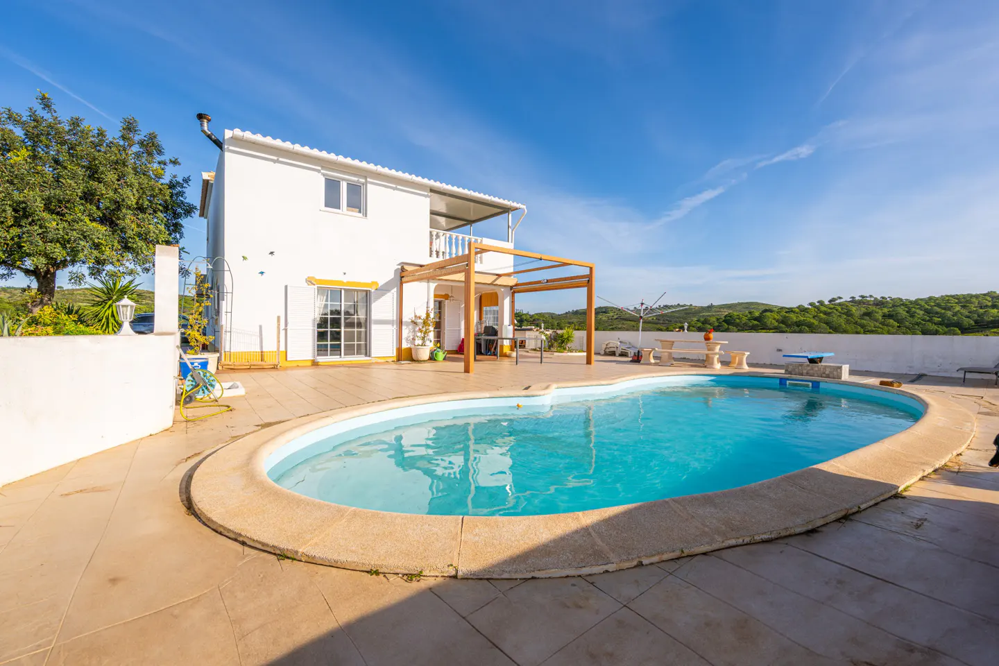 A white two-story house with a blue oval pool in the foreground under a clear blue sky.