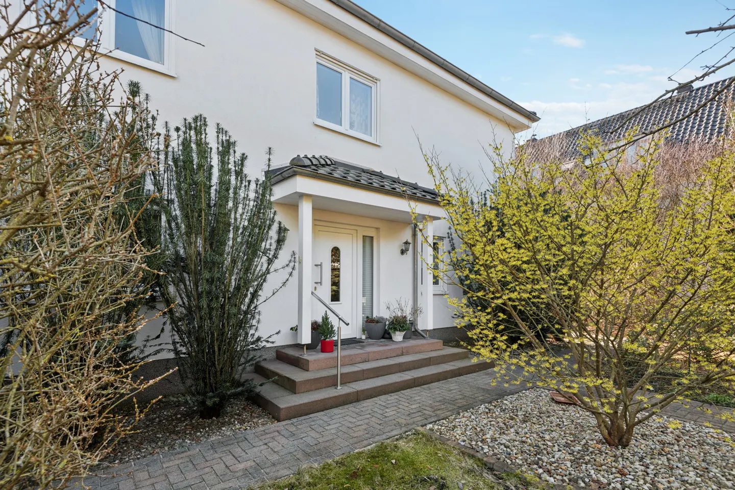 Exterior of a two-story white house with a covered porch, steps, and landscaping.