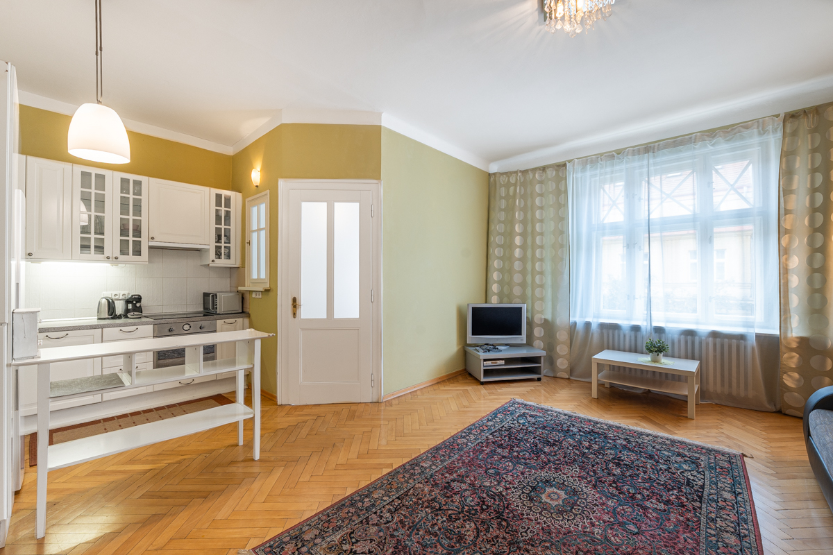 Open-plan kitchen and living area with white cabinets, yellow walls, herringbone wood floors, and a patterned area rug. [AI-generated text]