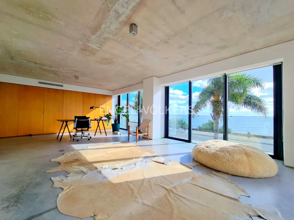 Bright, modern office space with a desk, chair, and large windows overlooking the ocean. A light-colored rug and beanbag add warmth.