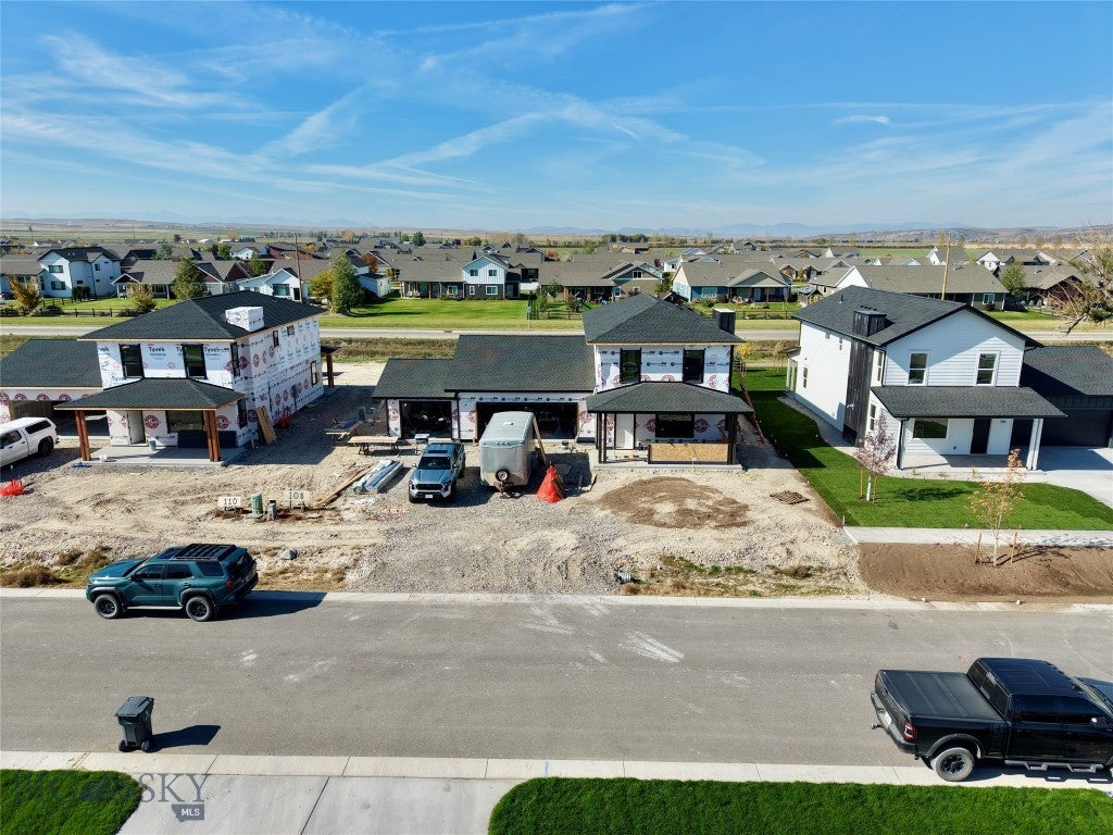 Aerial view of a suburban street with new homes under construction, featuring unfinished exteriors and parked vehicles. [AI-generated text]
