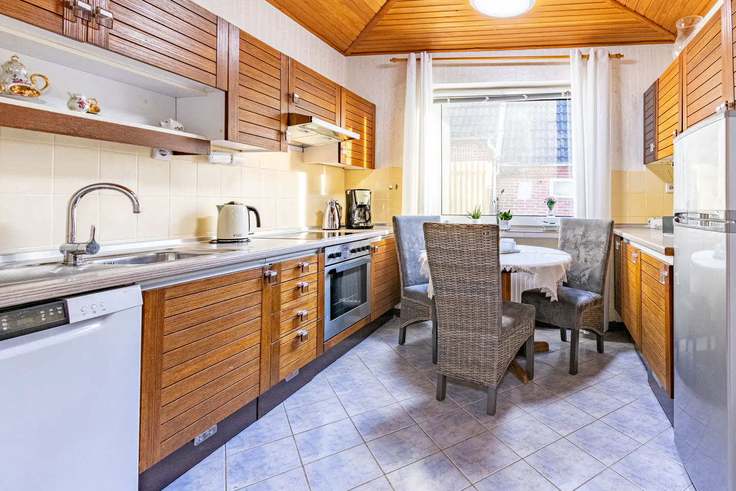 A kitchen with wood cabinets, a white dishwasher, a sink, and a round table with three chairs.